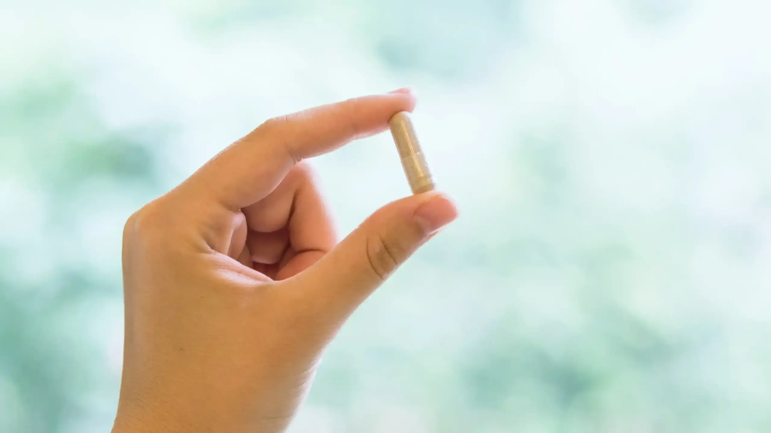 close-up of a hand gently holding a supplement capsule