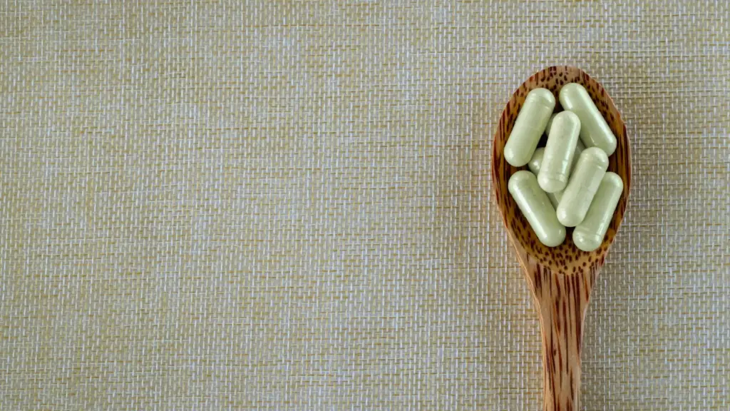 A wooden spoon resting on a flat surface, filled with supplement capsules