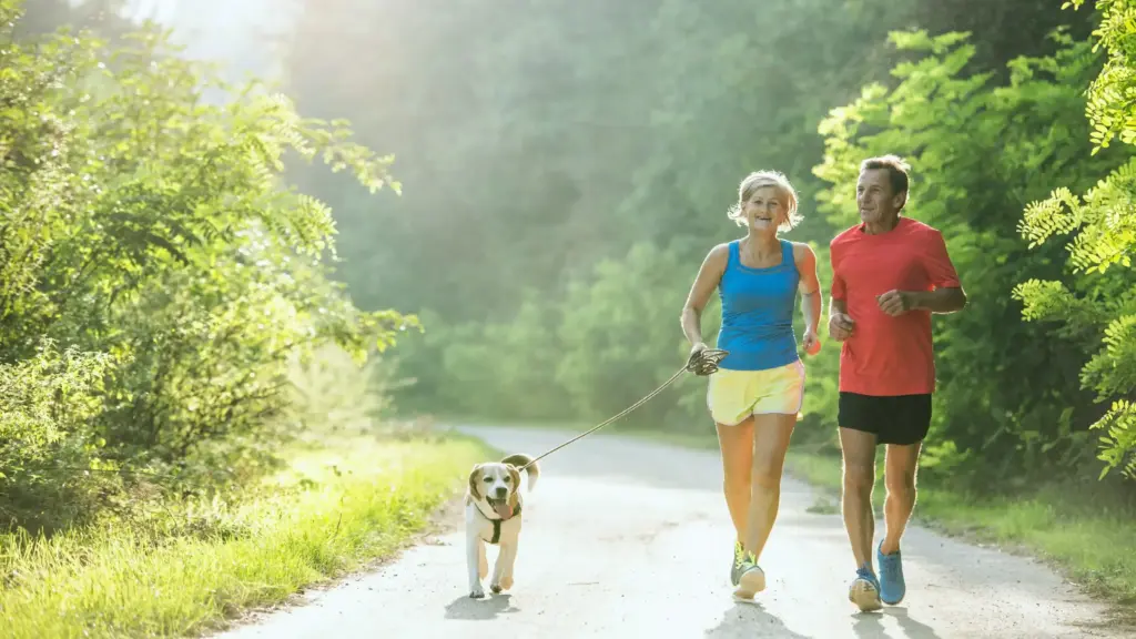 A middle-aged couple jogging side by side along a scenic trail
