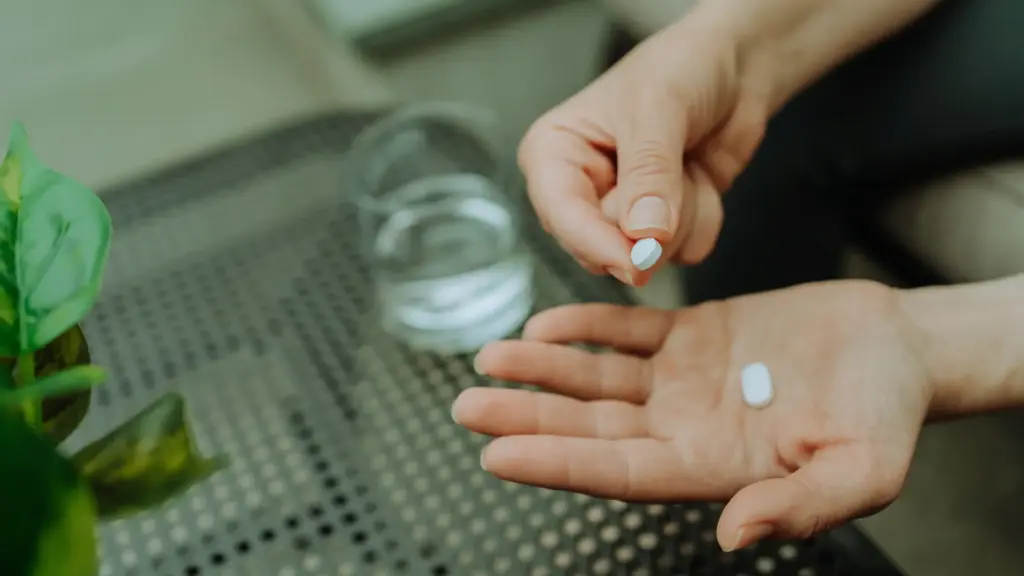 A man holding supplement capsules in his palm with a glass of water placed beside him